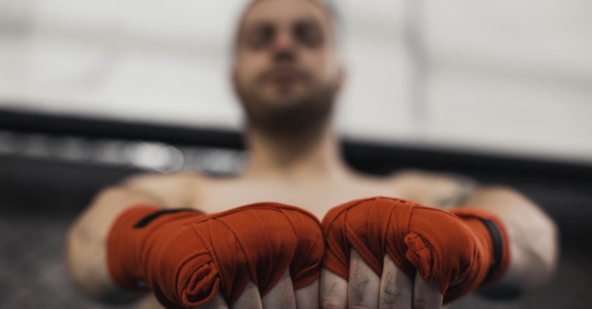 A fighter holds out both fists in orange hand wraps toward the camera