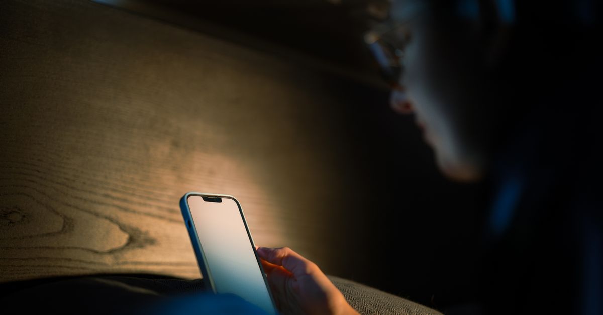 A hand holding a smartphone with a lit screen in a dark room