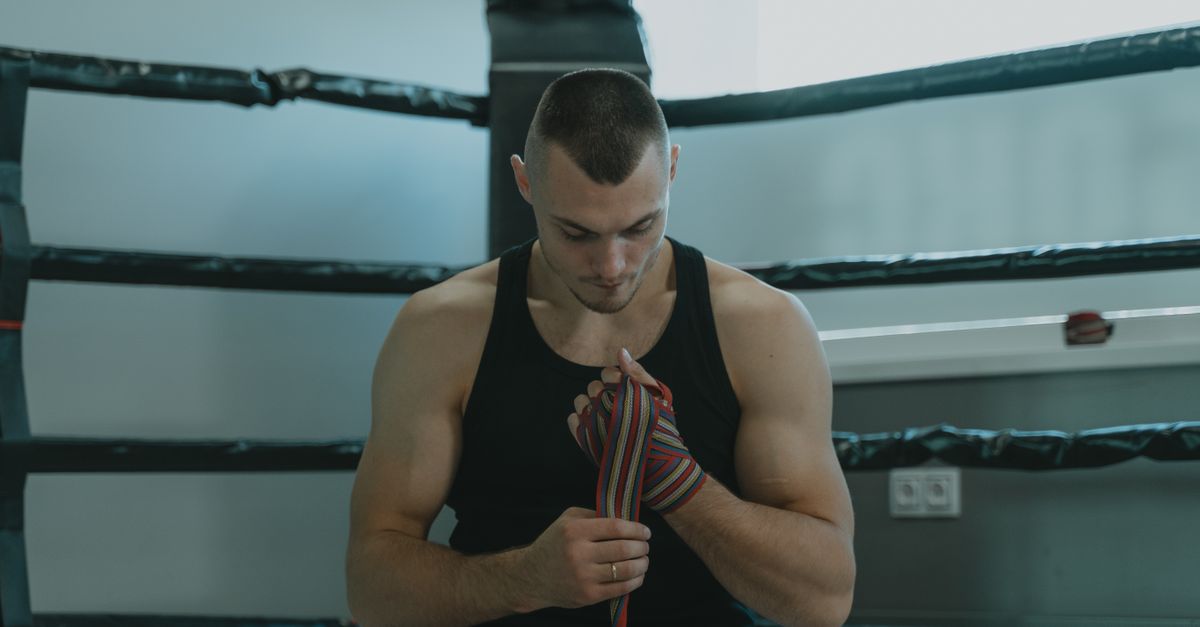 A fighter in a black vest wrapping his hands in the corner of a boxing ring