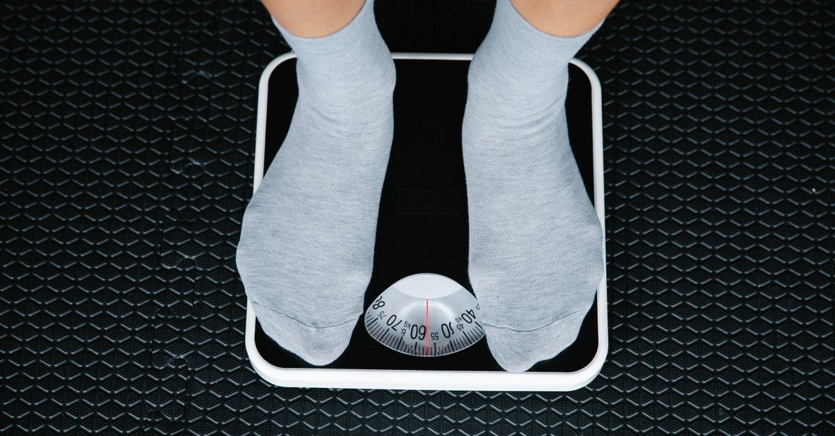 Feet in grey socks standing on a bathroom scale with a dial marked in kilograms